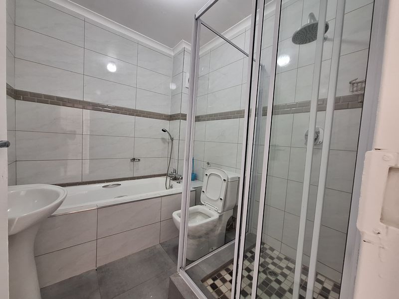 A modern, well-maintained bathroom featuring a separate bathtub, glass-enclosed shower, pedestal basin, and toilet with neutral wall and floor tiling.