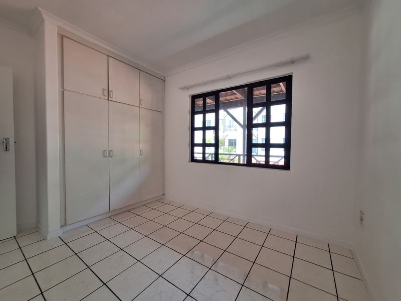 A bright, empty bedroom featuring built-in cupboards, tiled flooring, and a distinctive grid-pattern window.