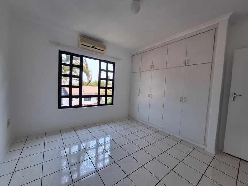 A bright, empty bedroom featuring white built-in cupboards, tiled flooring, and an installed air conditioning unit.