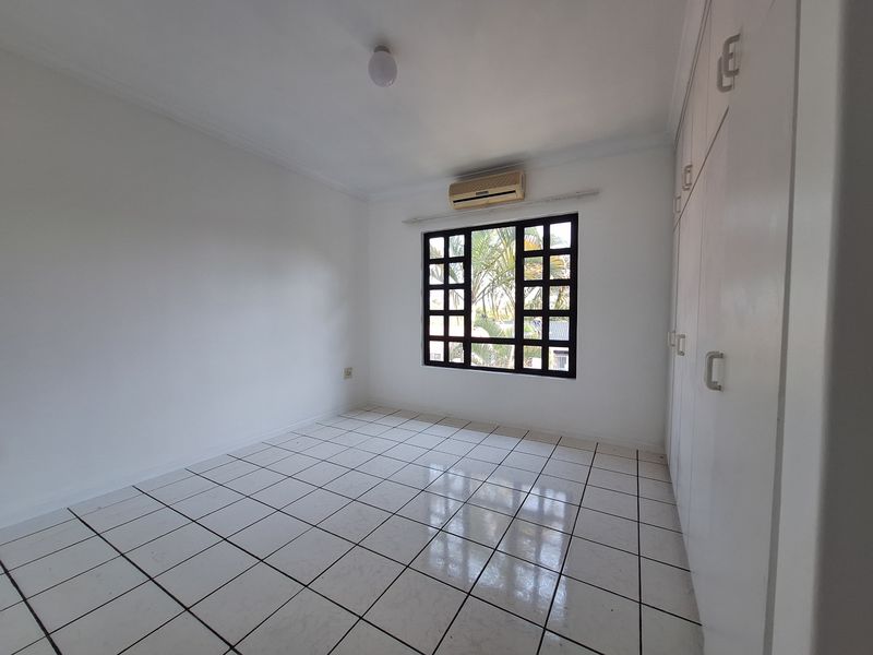 A bright, empty bedroom featuring white tiled flooring, built-in cupboards, and a wall-mounted air conditioning unit.