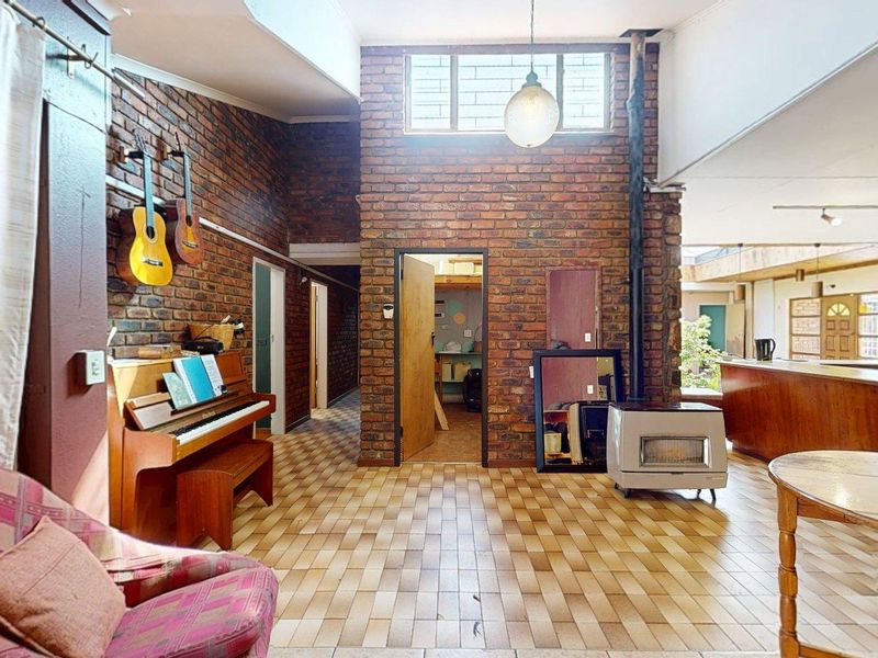Spacious open-plan living area featuring exposed brick walls, high ceilings with clerestory windows, tiled flooring, and a built-in fireplace.