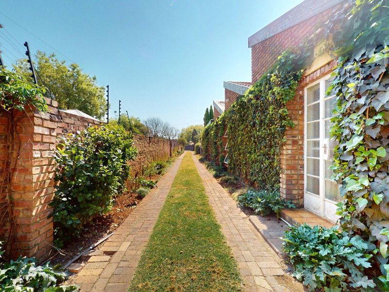 A narrow, well-maintained brick-paved garden path lined with established ivy-covered brick walls and electric security fencing.