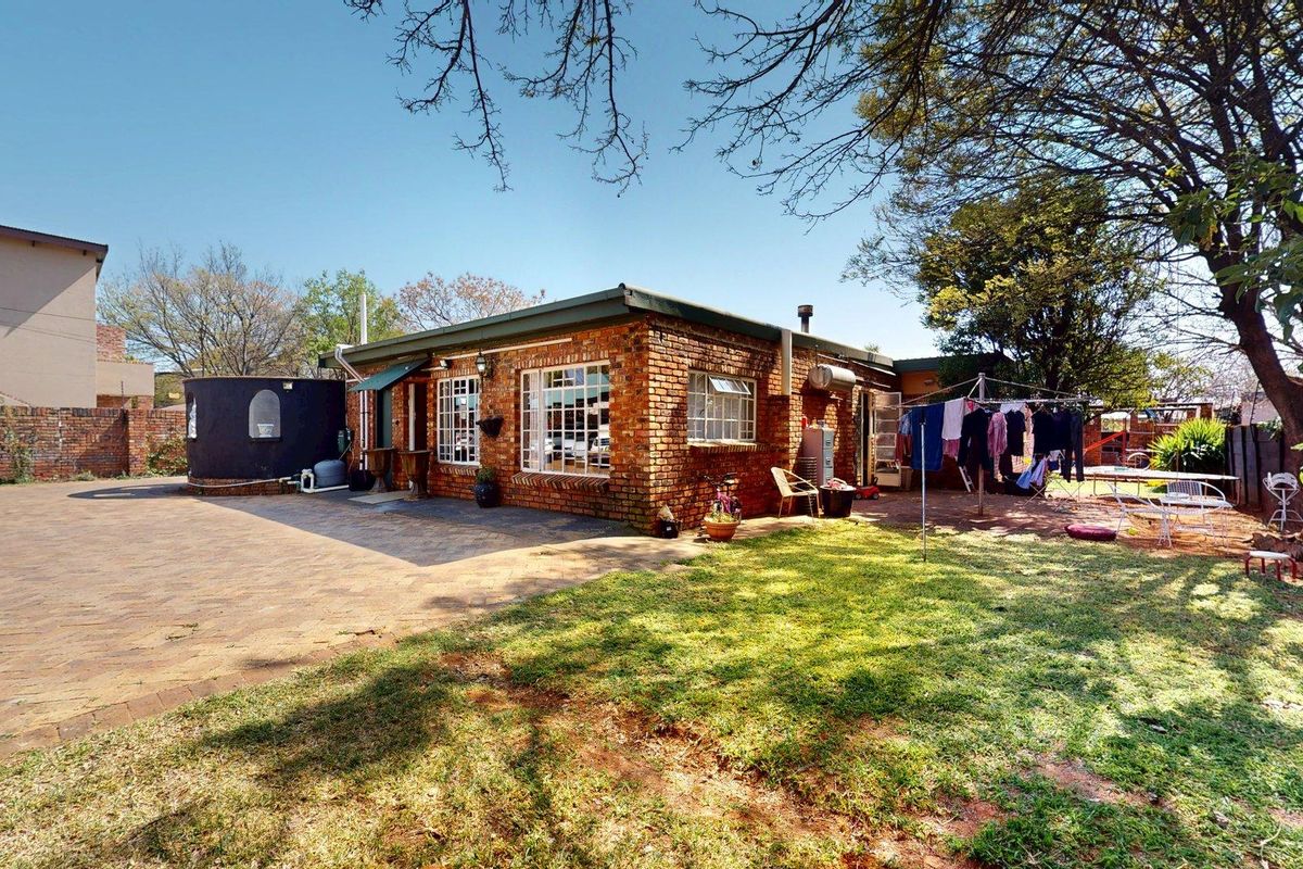 Rear view of a face brick house featuring a paved driveway, established lawn, and a water tank.