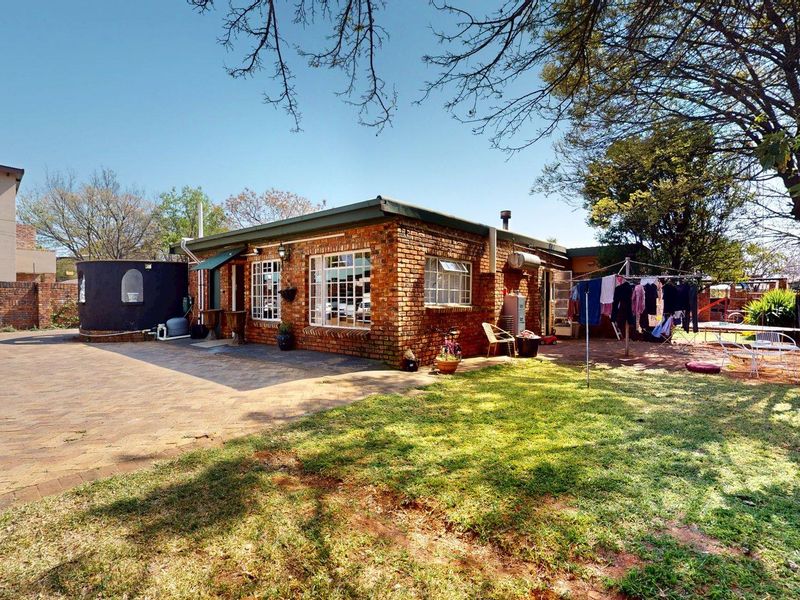 Rear view of a face brick house featuring a paved driveway, established lawn, and a water tank.