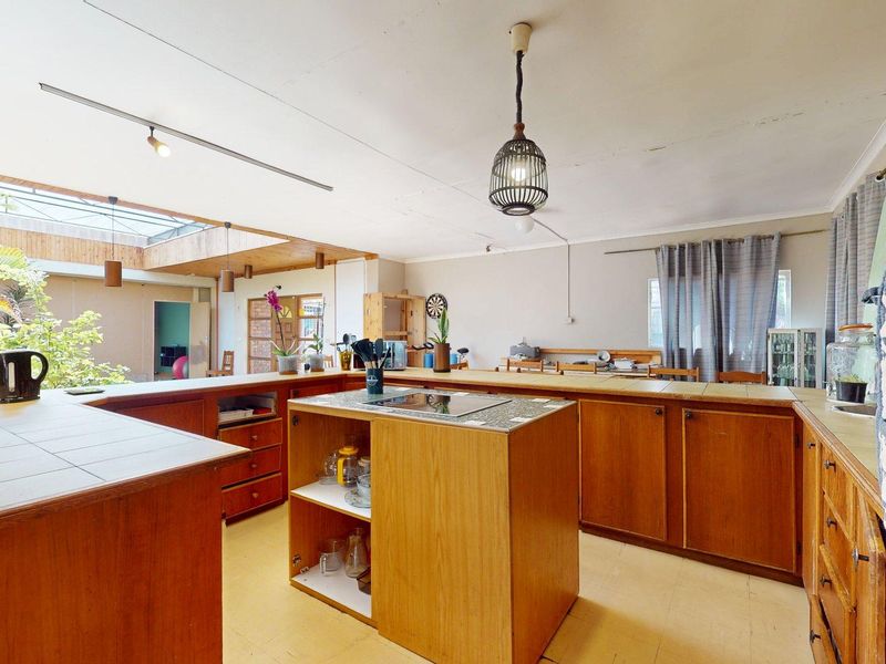 Spacious kitchen featuring extensive wooden cabinetry, tiled countertops, a central island with a hob, and a large skylight providing natural light.