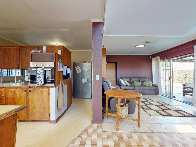Open-plan kitchen and living area featuring dated wooden cabinetry, built-in oven, tiled flooring, and direct access to the outdoor patio through sliding glass doors.