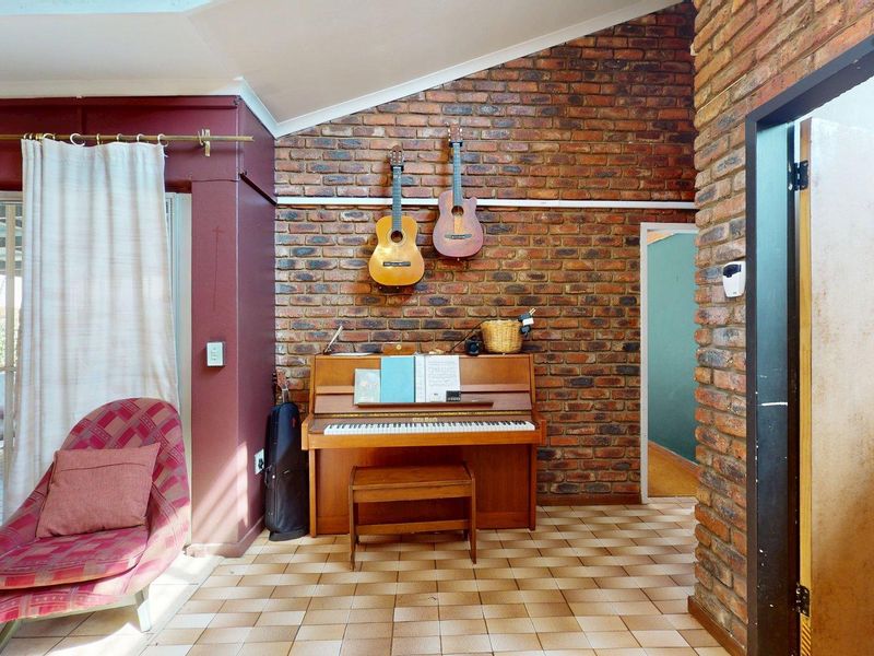 Living area featuring an exposed brick feature wall, vaulted ceiling, and tiled flooring with direct access to an outdoor patio through sliding glass doors.