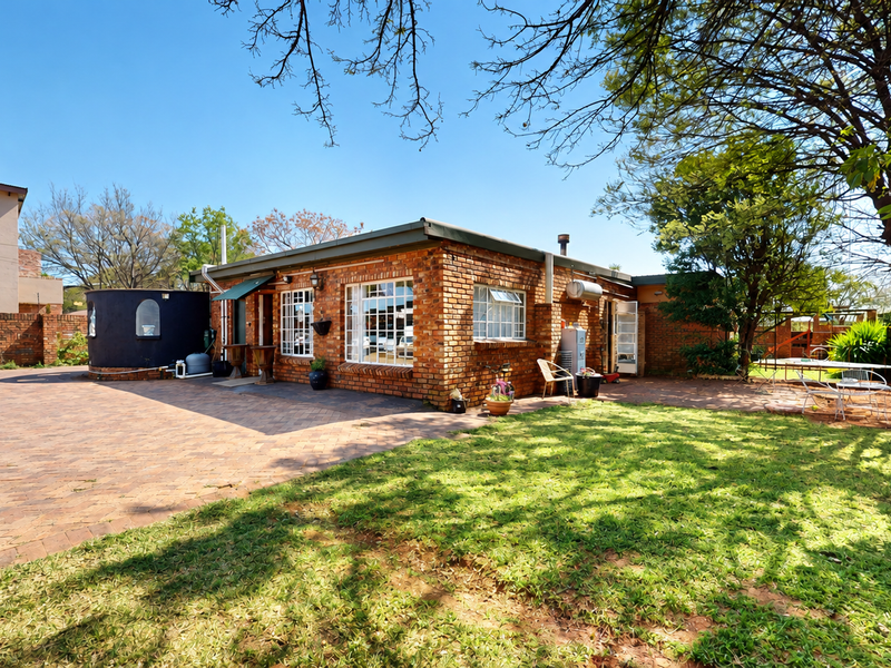 Rear view of the property featuring a brick facade, paved courtyard area, established lawn, and a water tank.