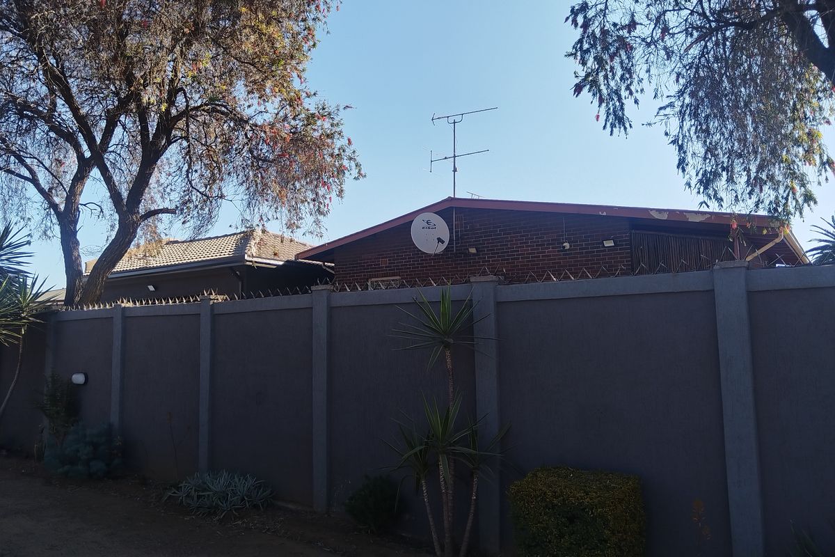 Rear view of the property featuring a brick facade, perimeter wall with security spikes, and roof-mounted satellite dish and antenna.