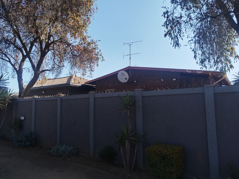Rear view of the property featuring a brick facade, perimeter wall with security spikes, and roof-mounted satellite dish and antenna.