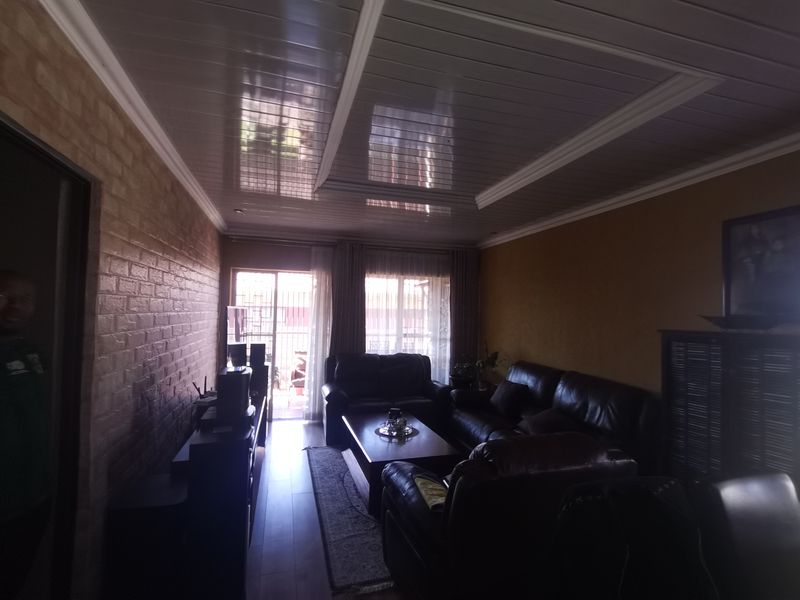 A living room featuring a glossy PVC ceiling, brick-effect wall cladding, and laminate flooring, with access to an outdoor area through a sliding glass door.