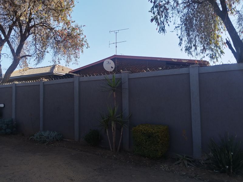 Front view of the property featuring a high perimeter wall with security spikes, satellite dish, and television antenna mounted on the brick structure.