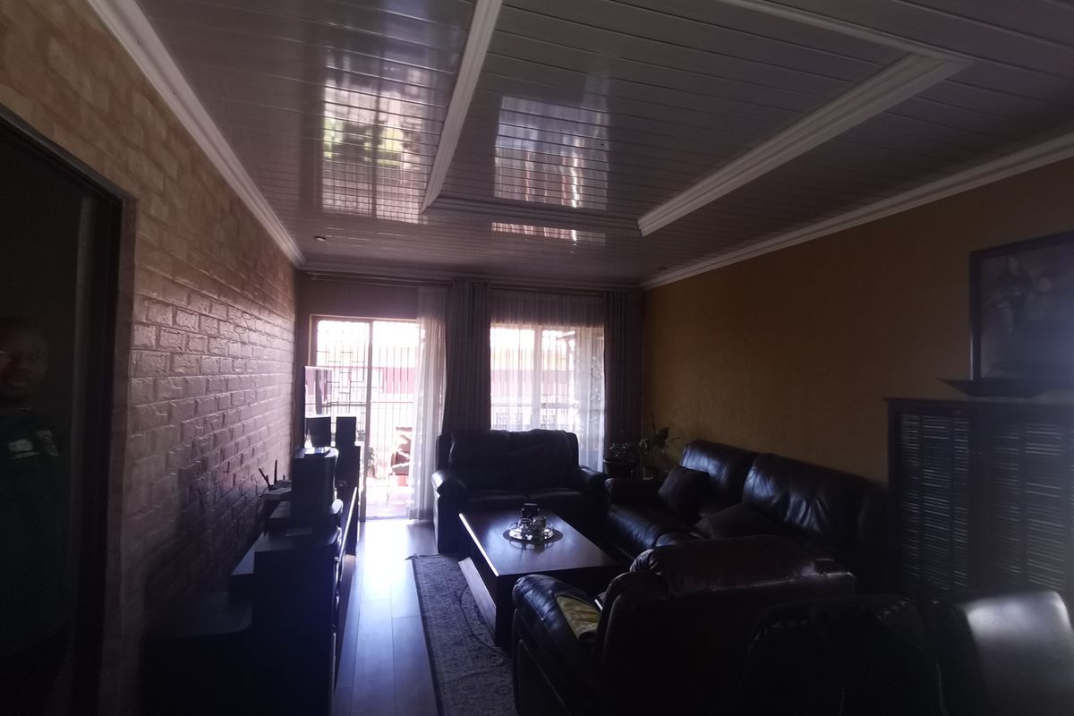 A living room featuring a glossy PVC ceiling, brick-effect wall cladding, and laminate flooring, with access to an outdoor area through a sliding glass door.