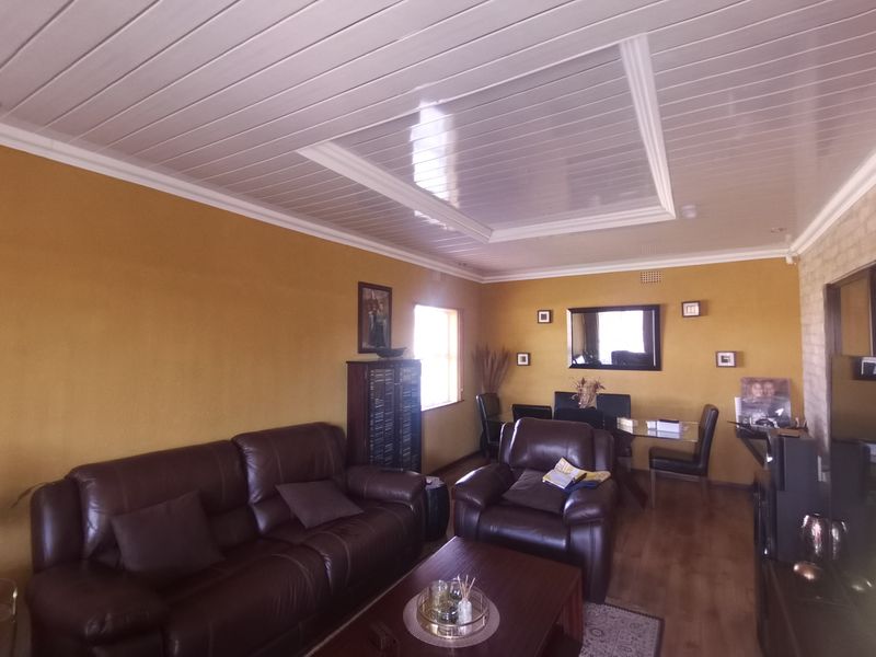 A living room featuring laminate flooring and a white PVC panelled ceiling with cove cornice detailing.