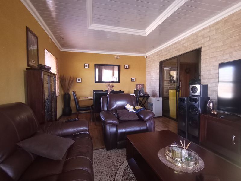 A living room featuring a coffered ceiling, laminate flooring, and an exposed brick feature wall with sliding glass door access to the exterior.