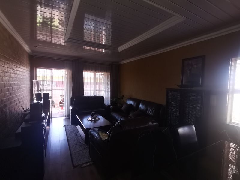 A living room featuring laminate flooring, an exposed brick feature wall, and a glossy panelled ceiling with access to an outdoor area.