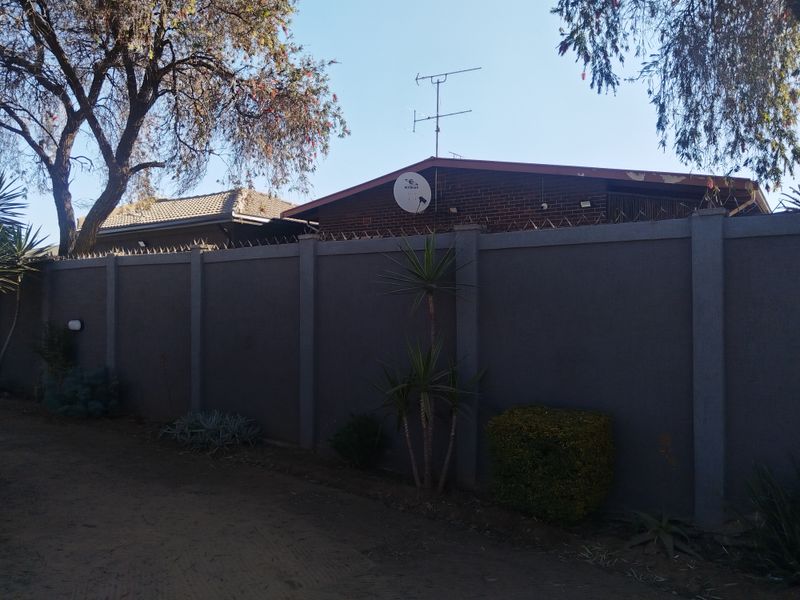 A view of the property's exterior front boundary wall, featuring security spikes, a satellite dish, and a roof antenna.