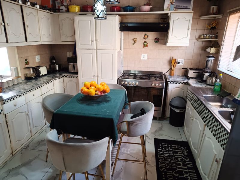 A functional kitchen featuring white cabinetry, a gas stove with extractor fan, double sink, and tiled finishes, offering a classic layout for daily meal preparation.