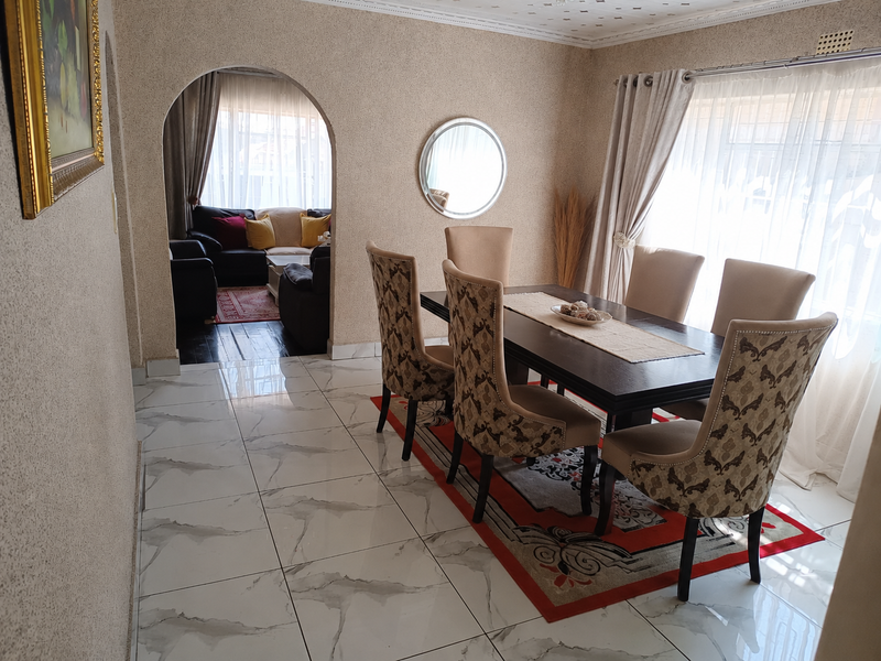 A well-maintained dining room featuring polished marble-look floor tiles, an arched entryway leading to the living area, and decorative ceiling detailing.