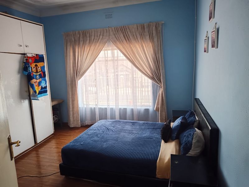 A bedroom featuring laminate flooring, a built-in wardrobe, and a large window with security bars, providing natural light.