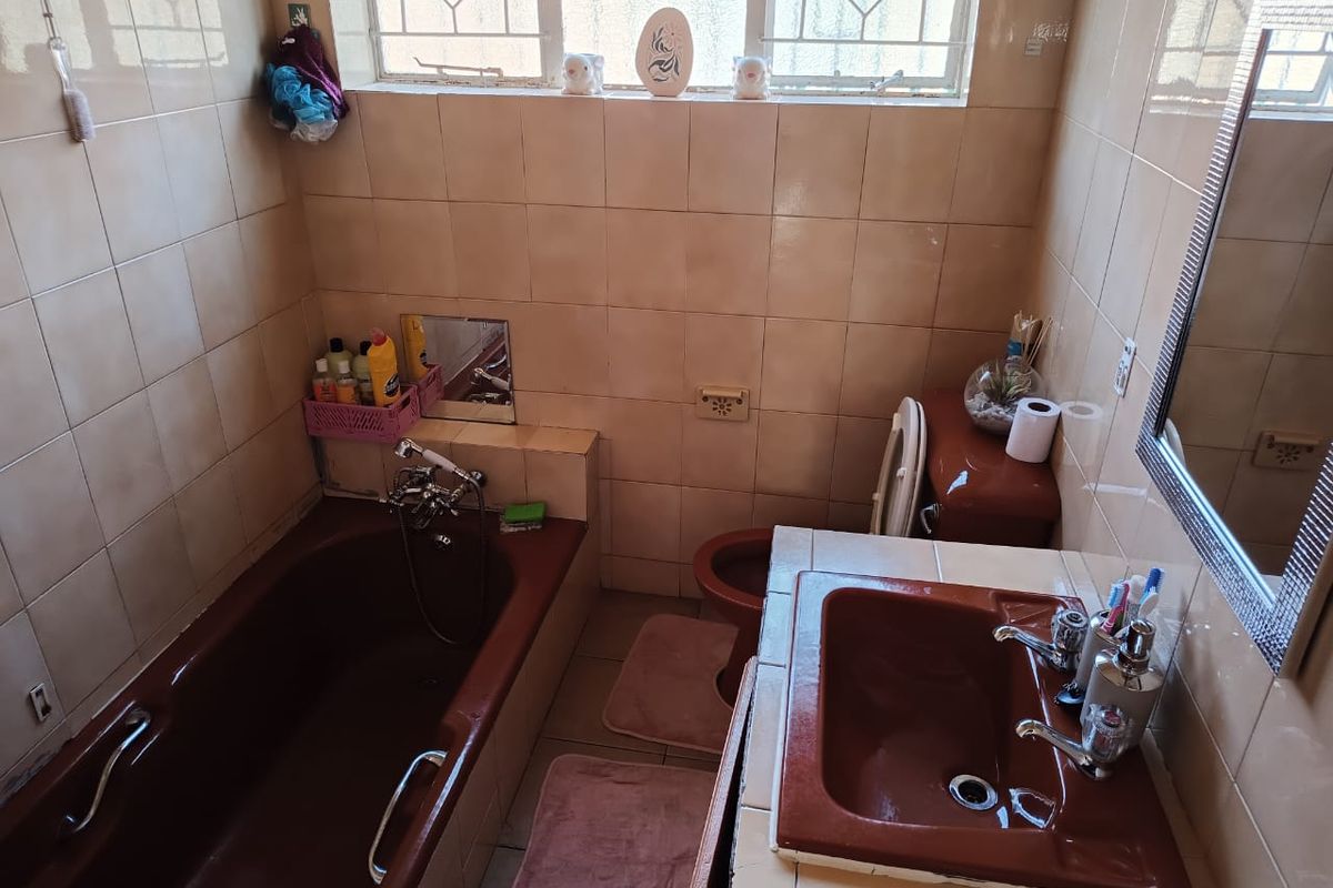 A dated bathroom featuring brown sanitaryware, tiled walls and floors, and a window with security bars.