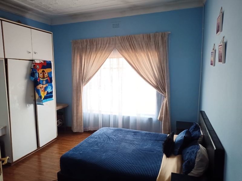 A bedroom featuring laminate flooring, a built-in wardrobe, and a large window with curtains.
