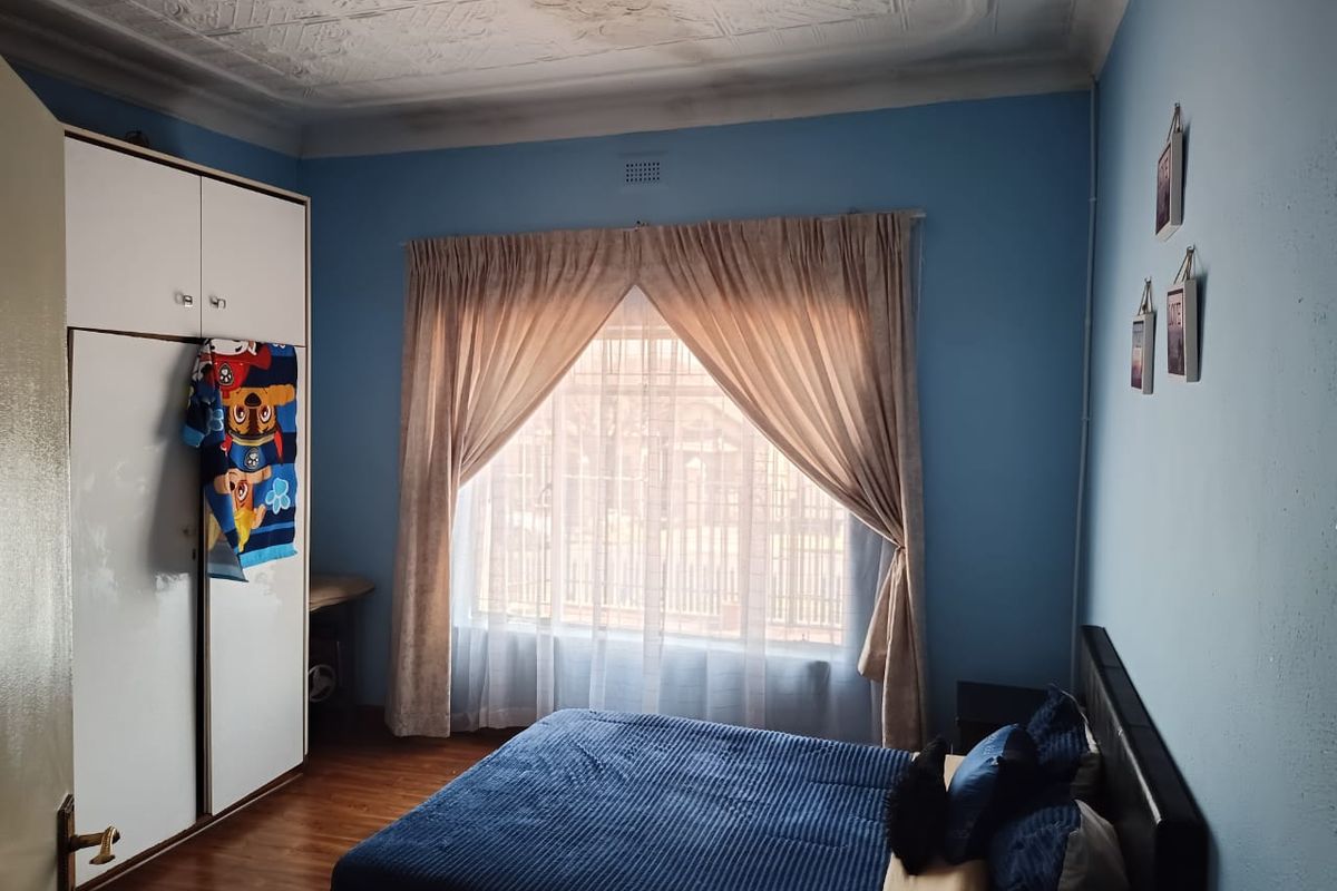 A bedroom featuring laminate flooring, a built-in wardrobe, and a decorative pressed metal ceiling with visible signs of water damage.