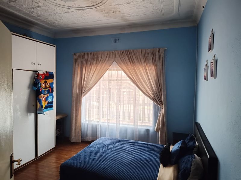 A bedroom featuring laminate flooring, a built-in wardrobe, and a decorative pressed metal ceiling with visible signs of water damage.