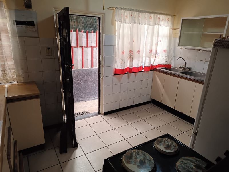 A functional kitchen featuring tiled flooring, a double sink, and built-in cabinetry with direct access to an exterior area via a security gate.
