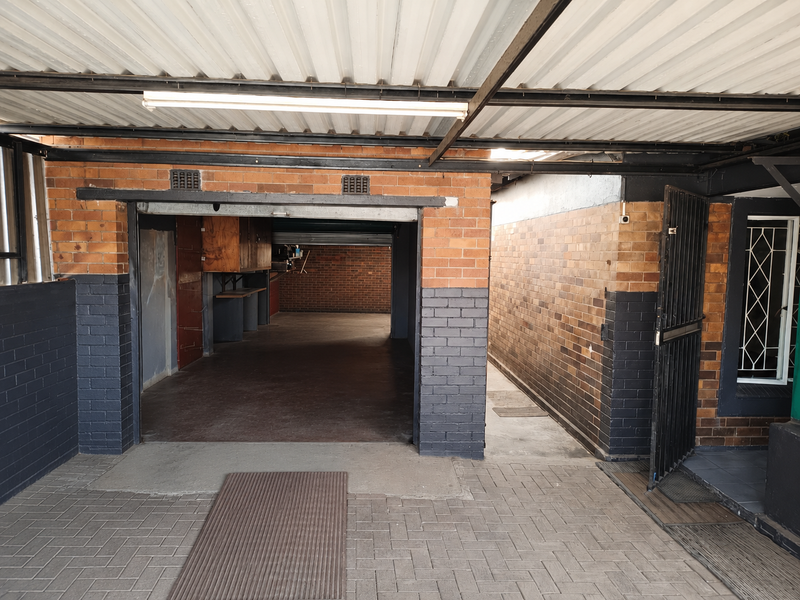 A spacious, covered garage area featuring brick walls, paved flooring, and secure access gates, providing ample space for vehicle storage.