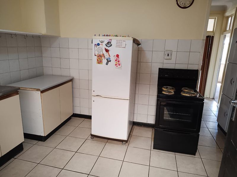A functional kitchen featuring tiled flooring, a tiled splashback, and built-in cabinetry with an integrated electric stove and oven.