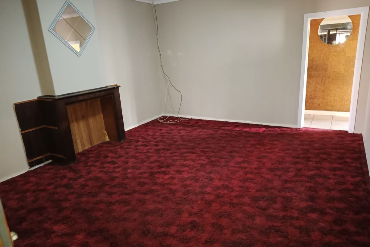An empty living room featuring a traditional fireplace mantel, coving, and patterned red carpeting, offering a blank canvas for renovation.