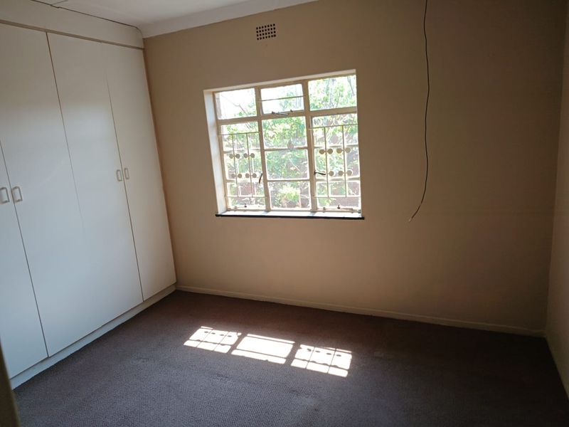 An empty bedroom featuring built-in cupboards, carpeted flooring, and a window with security bars. The room requires minor electrical finishing.