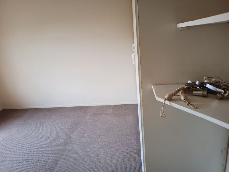 An empty bedroom featuring neutral walls, carpeted flooring, and a built-in cupboard for storage.
