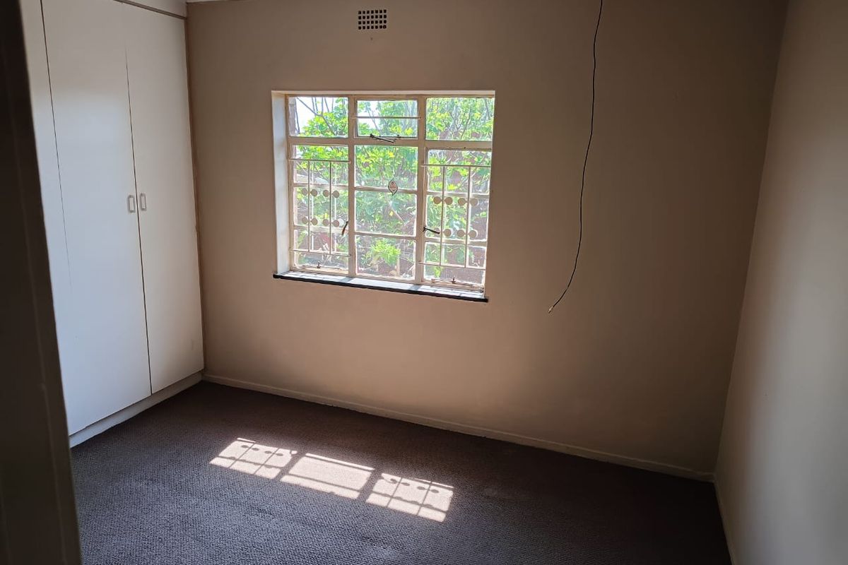 An empty bedroom featuring built-in cupboards, carpeted flooring, and a steel-framed window with security bars. Requires minor electrical finishing.