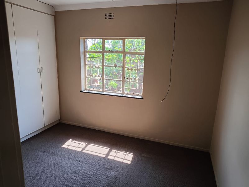 An empty bedroom featuring built-in cupboards, carpeted flooring, and a steel-framed window with security bars. Requires minor electrical finishing.