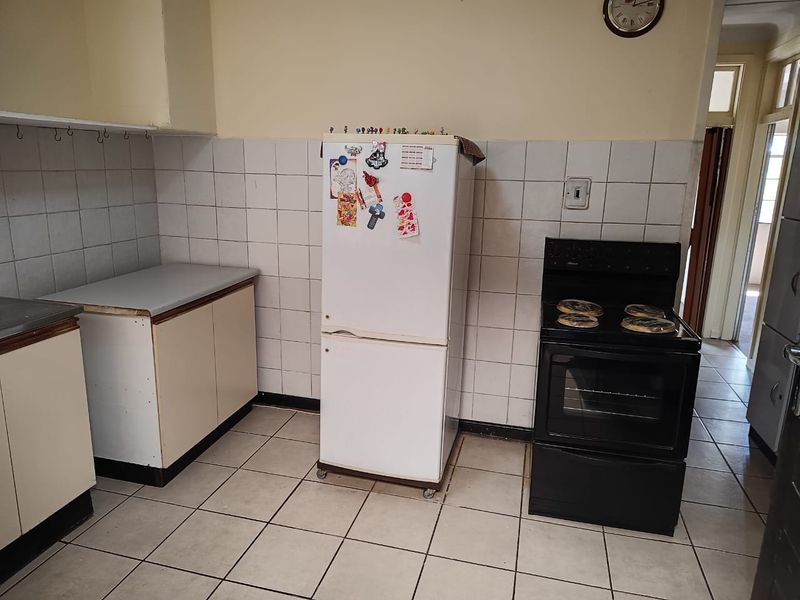 A functional kitchen featuring tiled flooring, a tiled splashback, and basic built-in cabinetry with a freestanding oven and hob.