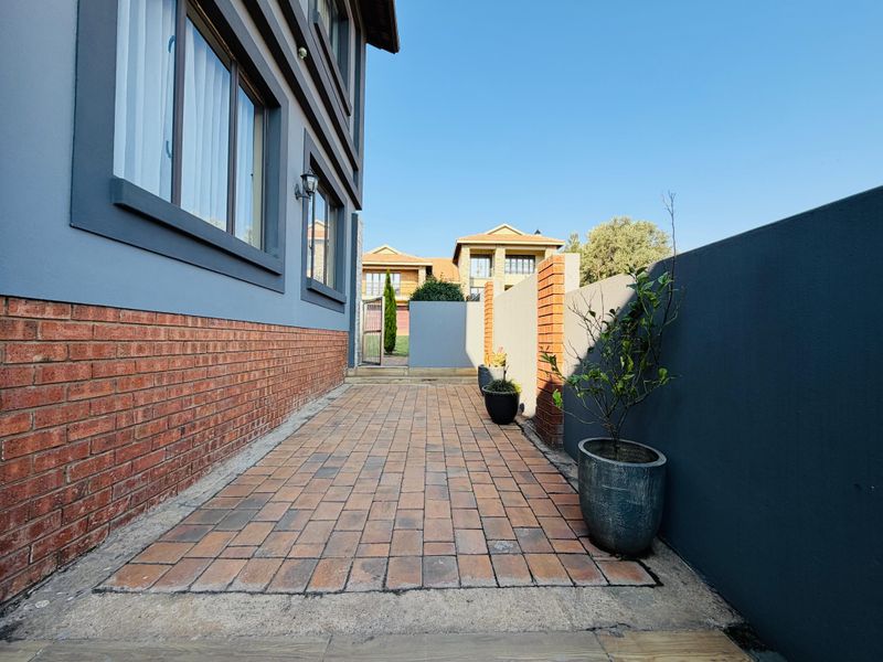 A clean side walkway featuring brick paving, a modern grey boundary wall, and a brick-accented exterior wall of the house.