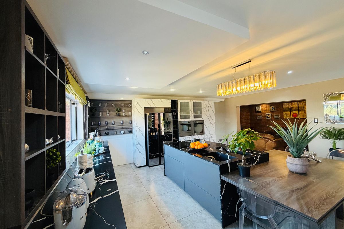 Modern kitchen featuring a large island with marble-look countertops, integrated appliances, sleek cabinetry, and stylish pendant lighting in an open-plan layout.