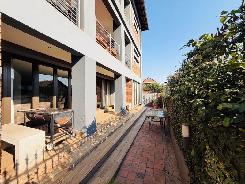 A multi-level outdoor patio area featuring timber decking, brick paving, and direct access to the interior through large sliding glass doors.