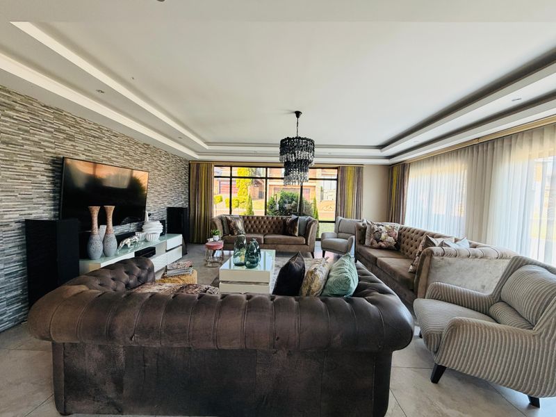 Spacious living room featuring a textured stone feature wall, recessed ceiling detail, large windows, and neutral tiled flooring.