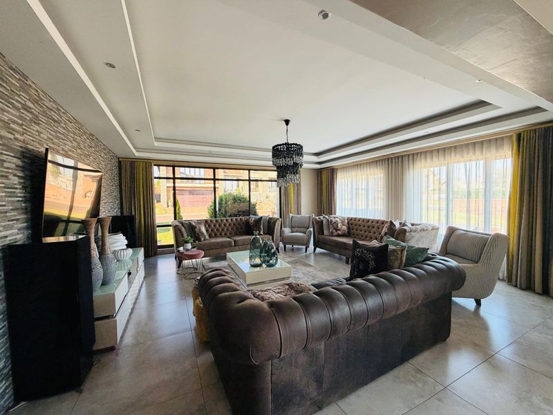 Spacious living room featuring a stone accent wall, recessed ceiling with downlights, and large windows providing ample natural light.