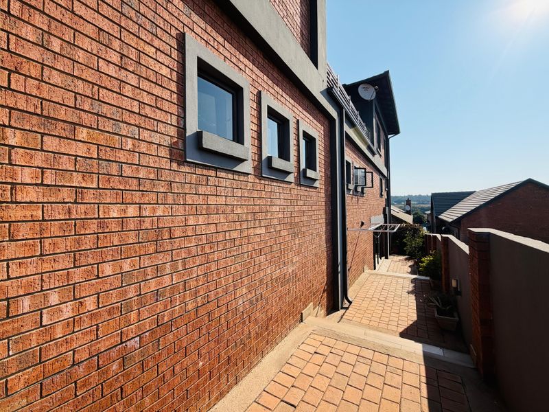 A side view of the property featuring a face brick facade, paved walkway, and boundary wall, showing well-maintained exterior finishes.