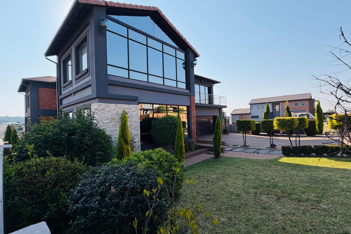 Modern double-story residence featuring a striking glass facade, stone cladding, and a well-maintained landscaped garden with paved driveway access.