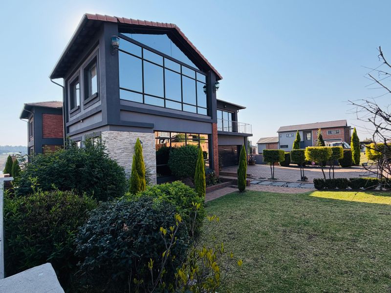 Modern double-story residence featuring a striking glass facade, stone cladding, and a well-maintained landscaped garden with paved driveway access.