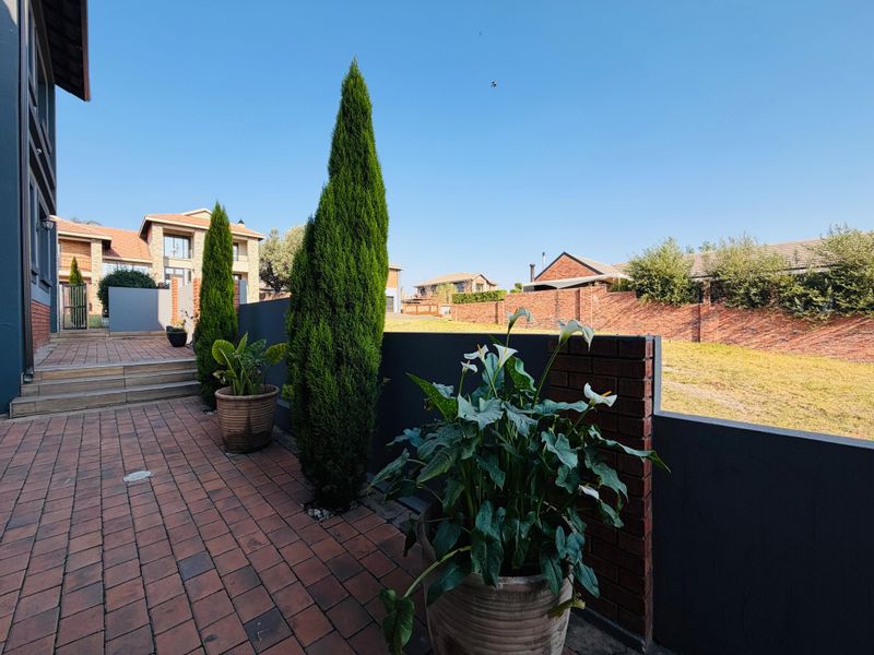 A well-maintained rear exterior area featuring brick paving, a solid brick boundary wall, and concrete steps leading to the main dwelling.