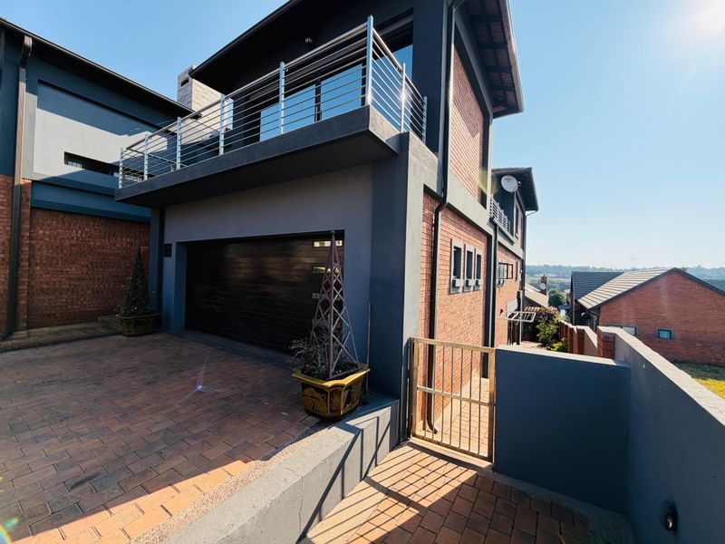Modern double-story home featuring a brick facade, integrated double garage, and an upper-level balcony with stainless steel railings.