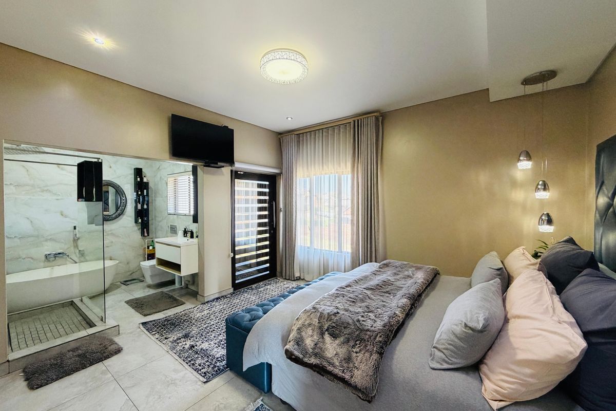 Spacious bedroom featuring an open-plan en-suite bathroom with a freestanding bathtub, glass shower, and modern wall-mounted vanity.