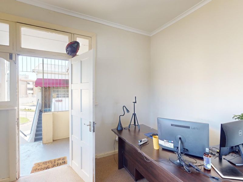 Entrance area featuring a timber panelled door with security gate and transom window, currently utilized as a home office space.