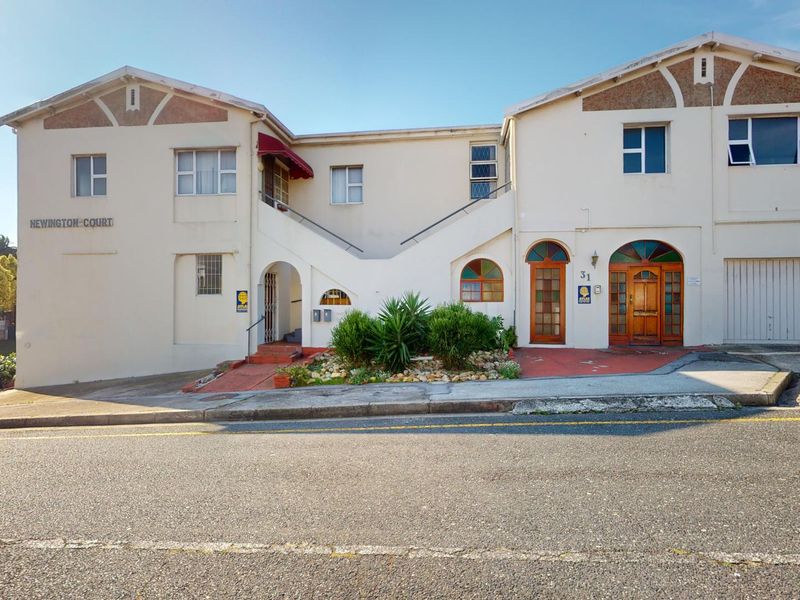 Front elevation of Newington Court apartment complex featuring a paved entrance area, external staircase, and secure garage access.